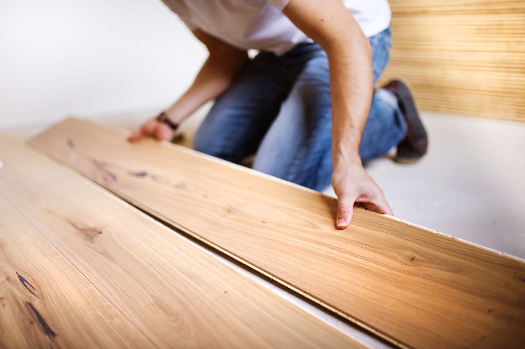 Close-up of a worker installing light oak wood flooring planks.